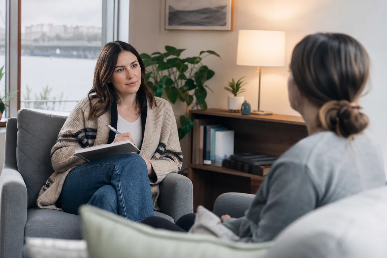 A therapist takes notes while listening to a client during a counseling session in a comfortable office.