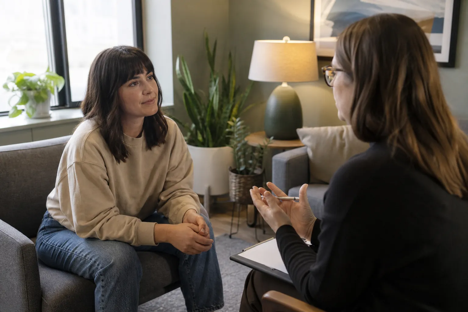 Woman Seated Across From an Open Notebook A woman sits on a sofa facing another woman holding an open notebook.